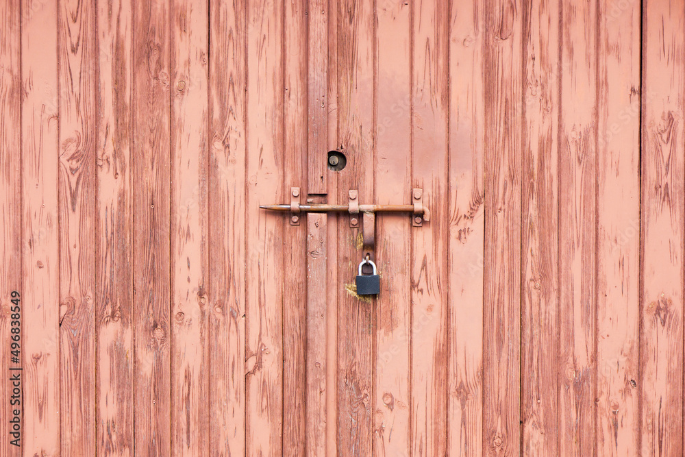 Wooden door background. Garage door texture. Abandoned locked gate. Metal padlock with peeling paint. Wooden door background. Garage door texture. Abandoned locked gate. Metal padlock with peeling paint.