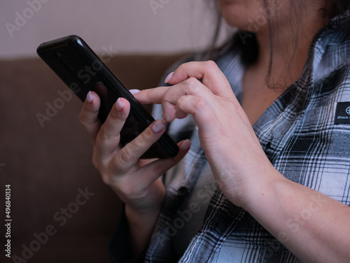 Tight shot of a woman's hands in a plaid shirt texting on the phone at home.