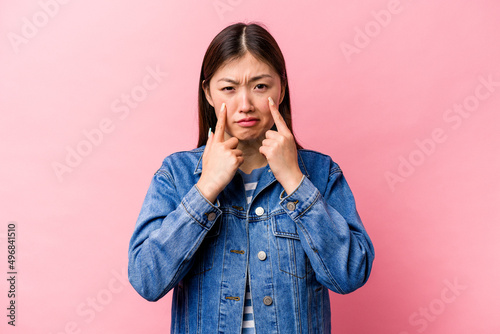 Young Chinese woman isolated on pink background crying, unhappy with something, agony and confusion concept.