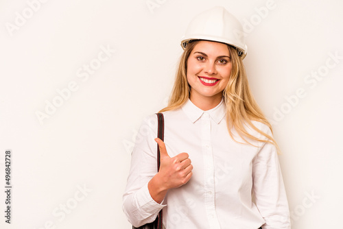 Young architect woman with helmet and holding blueprints isolated on white background smiling and raising thumb up