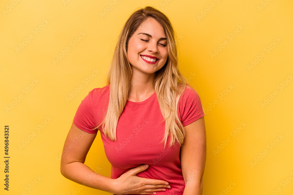 Obraz premium Young caucasian woman isolated on yellow background touches tummy, smiles gently, eating and satisfaction concept.