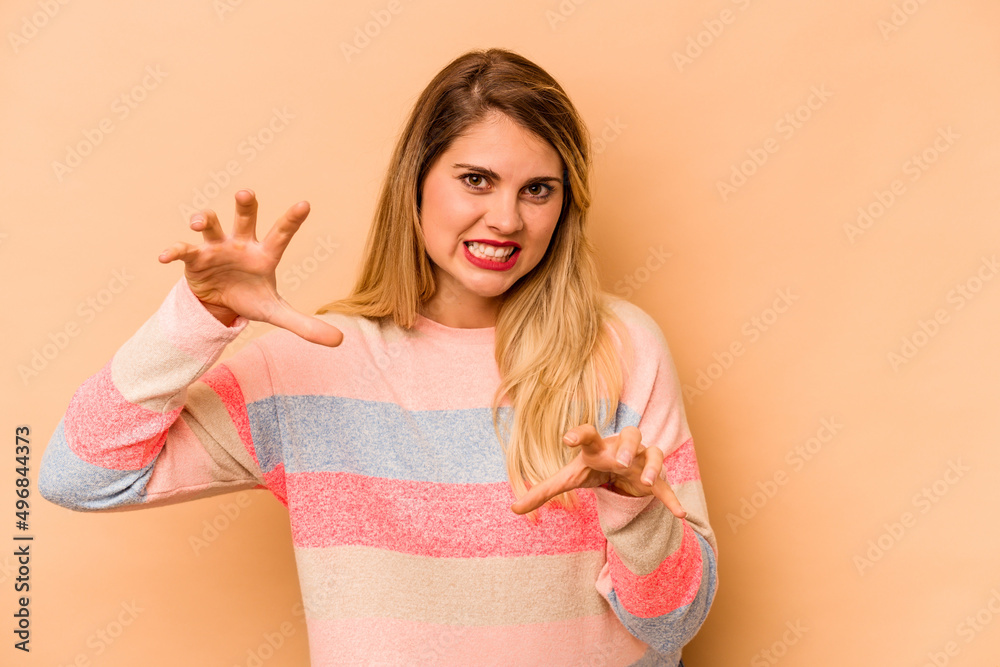 Young caucasian woman isolated on beige background showing claws imitating a cat, aggressive gesture. Young caucasian woman isolated on beige background showing claws imitating a cat, aggressive gesture.