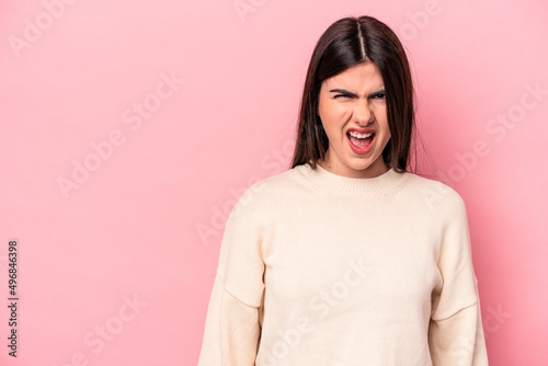 Young caucasian woman isolated on pink background shouting very angry, rage concept, frustrated. © Asier