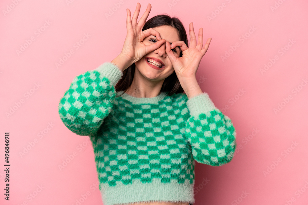 Young caucasian woman isolated on pink background showing okay sign over eyes