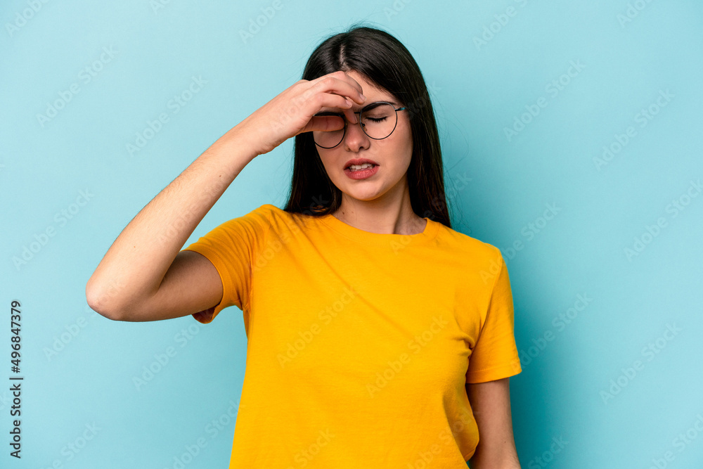 Young caucasian woman isolated on blue background having a head ache, touching front of the face. Young caucasian woman isolated on blue background having a head ache, touching front of the face.