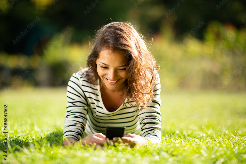 smiling young woman lying on grass in park looking at cellphone smiling young woman lying on grass in park looking at cellphone