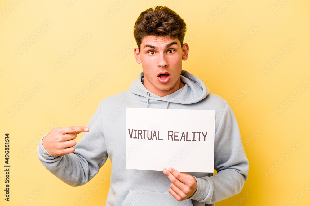 Young caucasian man holding virtual placard isolated on yellow background pointing to the side Young caucasian man holding virtual placard isolated on yellow background pointing to the side