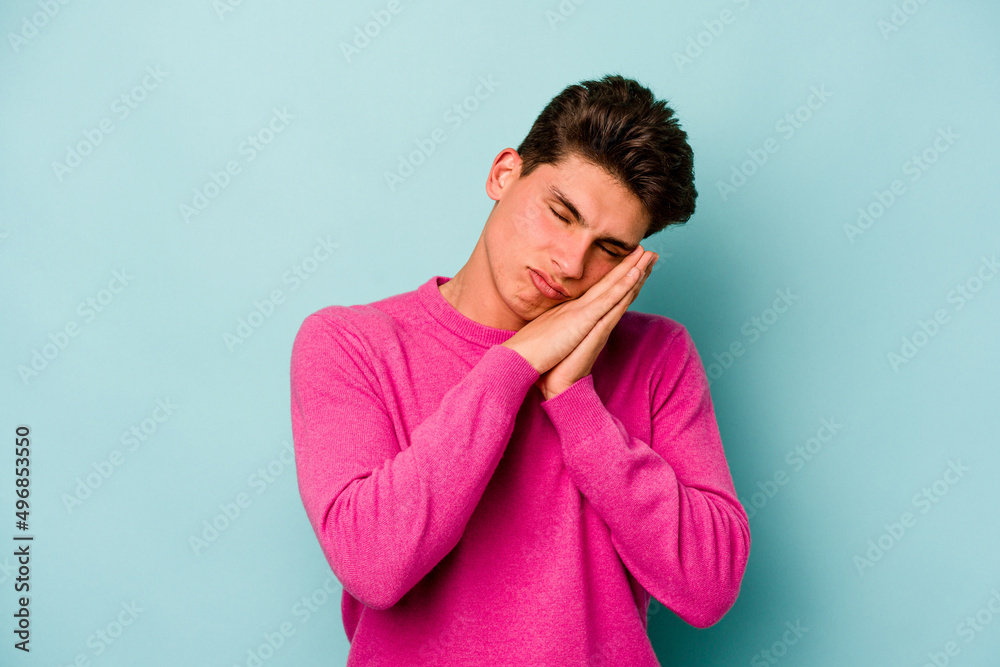 Young caucasian man isolated on blue background yawning showing a tired gesture covering mouth with hand. Young caucasian man isolated on blue background yawning showing a tired gesture covering mouth with hand.