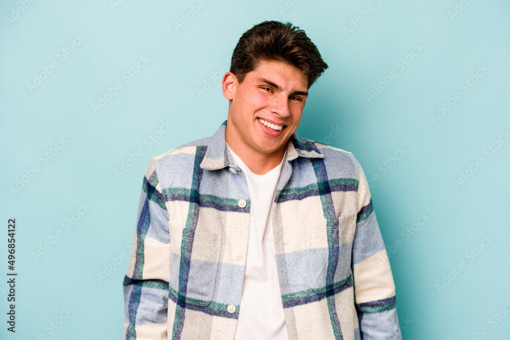 Fototapeta premium Young caucasian man isolated on blue background laughs and closes eyes, feels relaxed and happy.