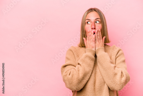 Young caucasian woman isolated on pink background thoughtful looking to a copy space covering mouth with hand.