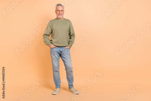 Full body photo of nice aged grey hairdo man stand wear eyewear pullover jeans shoes isolated on beige background