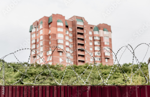 Barbed wire on fence with modern residential building on background. Protection and prohibition concept.
