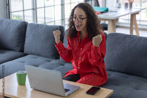 young freelance woman sitting on sofa at home smile and rejoice at success while using his laptop