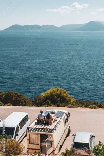 Fototapeta Naklejka Na Ścianę i Meble -  Family traveling with motorhome are eating breakfast on a beach. Travelers on an active family vacation with motorhome RV parked on the beach under a tree facing the sea, Crete, Greece.