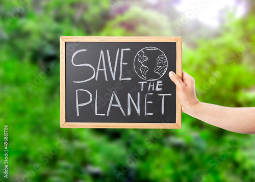 Closeup shot of a man's hand holding a blackboard sign that says SAVE THE PLANET in the woods