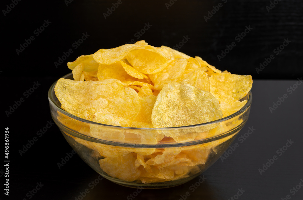 Crispy potato chips in white bowl with black background Crispy potato chips in white bowl with black background