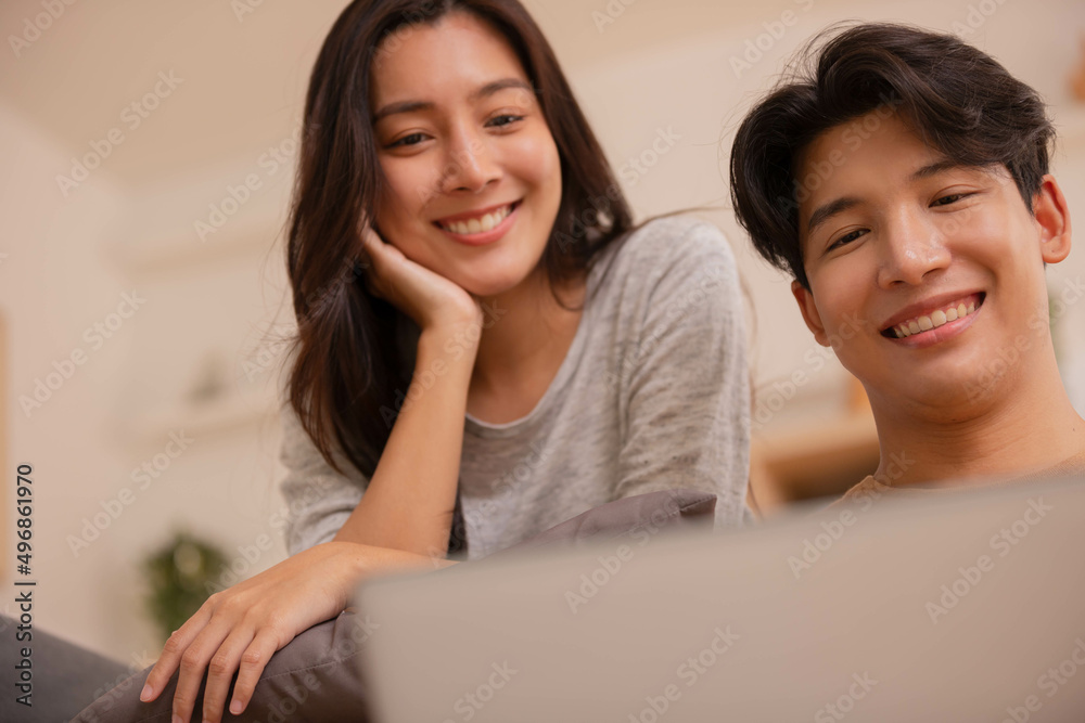 At home in the living roomm.Asian couple working and researching online on labtop while sitting on sofa. At home in the living roomm.Asian couple working and researching online on labtop while sitting on sofa.