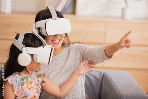 Asian mom and daughter wearing virtual reality headset listening to music and games sitting on sofa.c