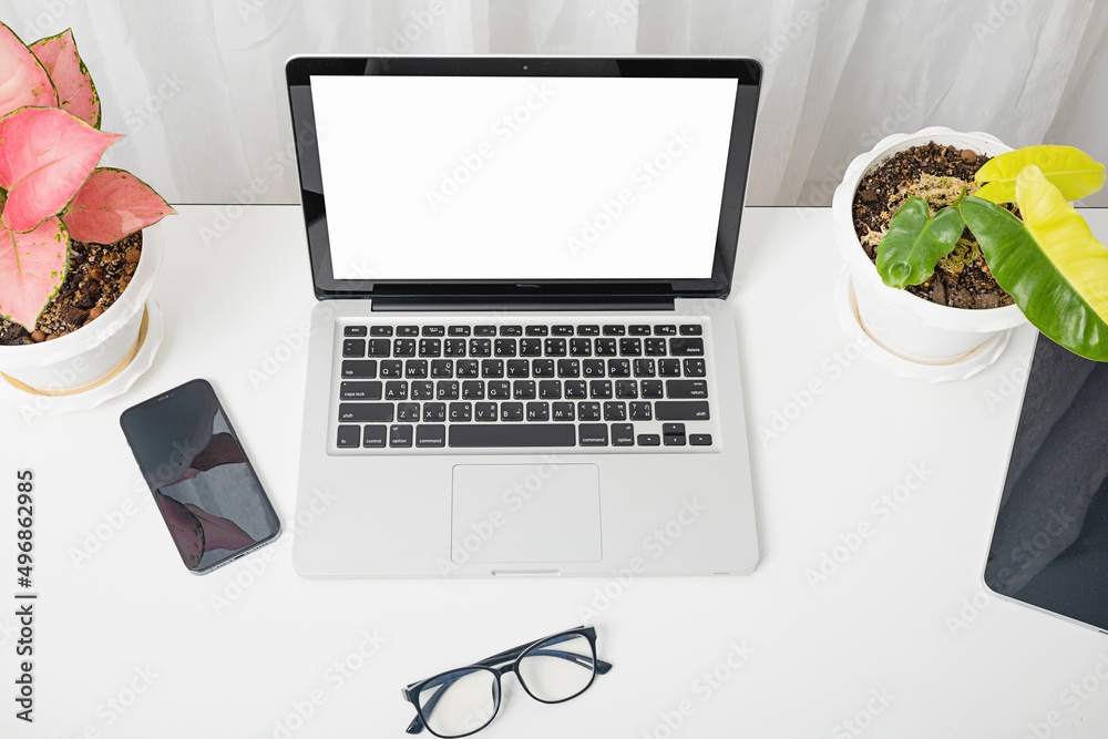 Modern workspace, mock up laptop computer blank white screen, eyeglasses and smartphone white table have potted plants on the desk, Notebook and mobile phone on desktop home office