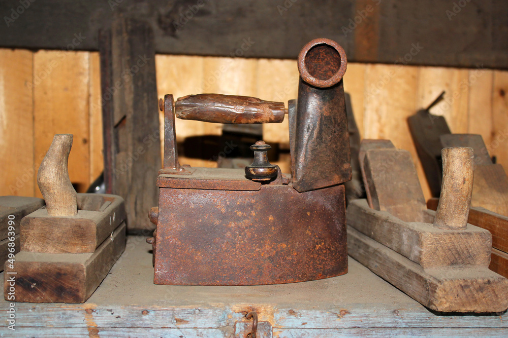 A set of household utensils and tools, including an old rusty charcoal iron with a pipe and wooden planers.
