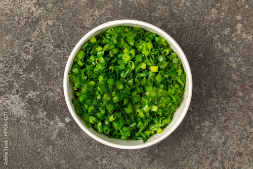A bowl of finely chopped green onions on gray textured background. Top view.