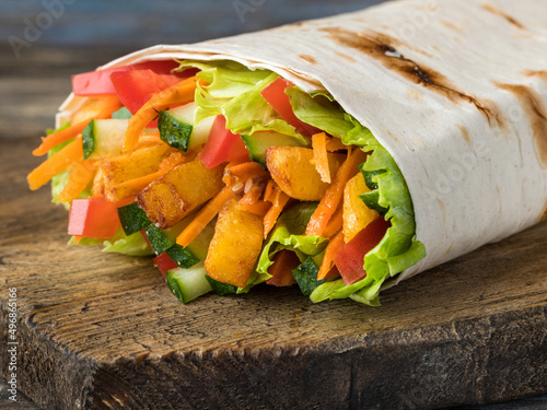 Vegetarian shawarma in lavash with cucumbers, potatoes, carrots, tomatoes, lettuce leaves. On a wooden brown background. Close up.