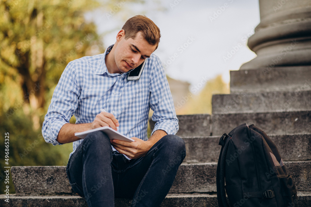 Obraz premium Handsome student sitting on stairs of university and studying