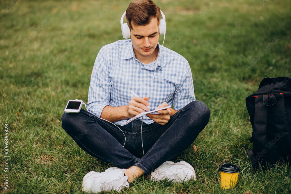 Obraz premium Young male student studying in park and sitting in park