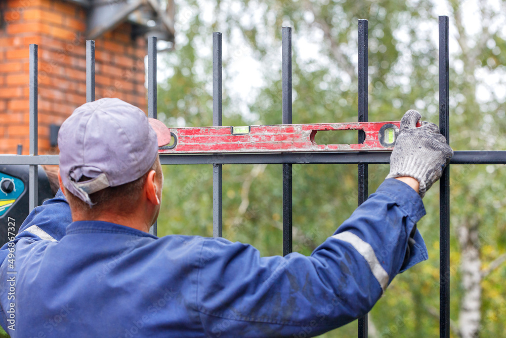 The builder uses an old level to level the metal fence when it is being installed. The builder uses an old level to level the metal fence when it is being installed.