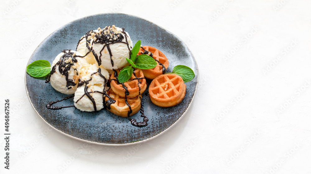 ice cream with waffles, chocolate syrup and fresh mint on a dark platter. copy space