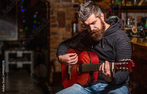 Live music. Guitars and strings. Bearded man playing guitar, holding an acoustic guitar in his hands. Music concept. Bearded guitarist plays. Play the guitar. Beard hipster man sitting in a pub