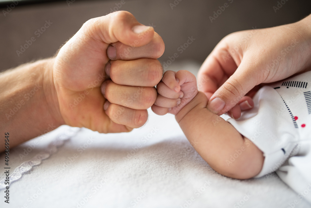 Fist of newborn baby and father with support of mother's hand, family photo, selective focus Fist of newborn baby and father with support of mother's hand, family photo, selective focus