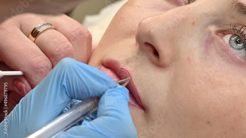 The cosmetologist makes permanent makeup on women's lips, outlines the contour of the lips with a red pen before the procedure.