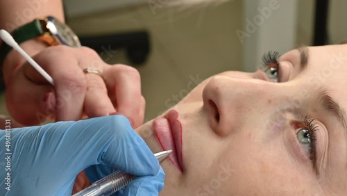 The cosmetologist makes permanent makeup on women's lips, outlines the contour of the lips with a red pen before the procedure.
