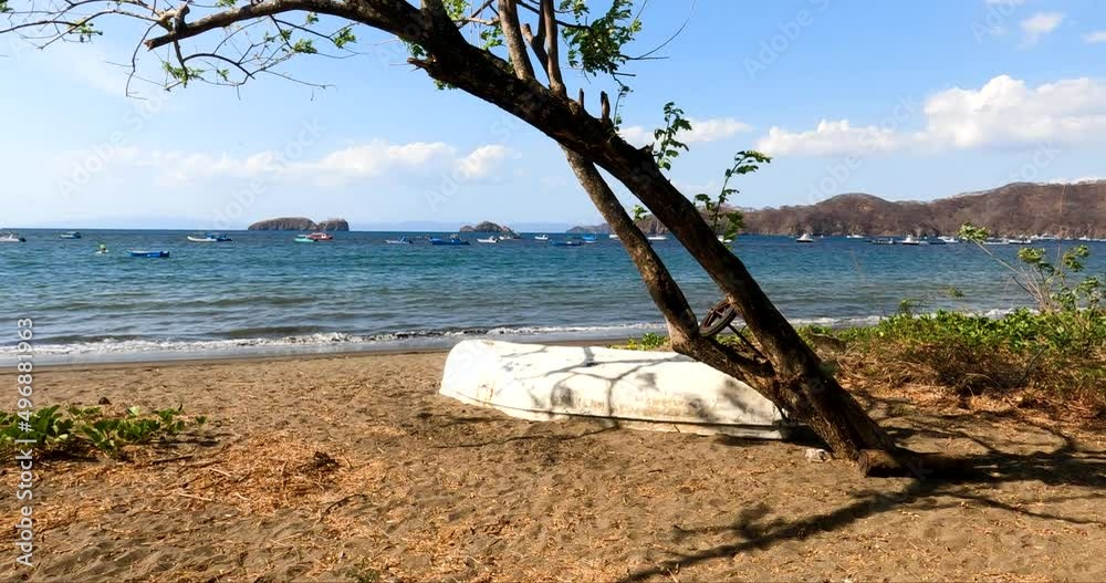 Wooden boat on tropical beach with a tree on a sunny day, Coco Beach in Guanacaste, Costa Rica. Panoramic View of Pacific Ocean with small islands and fishing boats Wooden boat on tropical beach with a tree on a sunny day, Coco Beach in Guanacaste, Costa Rica. Panoramic View of Pacific Ocean with small islands and fishing boats