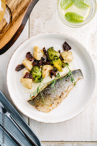 Grilled Sea bass with creamy lemon sauce and vegetables, cauliflower, broccoli, sun-dried tomatoes. top view