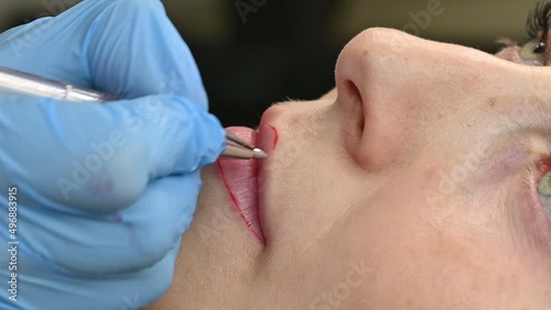 The cosmetologist makes permanent makeup on women's lips, outlines the contour of the lips with a red pen before the procedure.