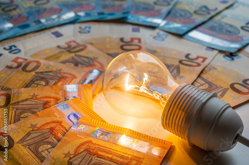 Light bulb turned on, with Euro banknotes around. Increase in electricity tariffs, energy dependence, energy sources and energy supplies.
