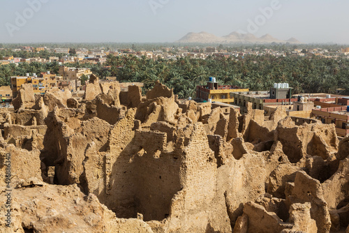 View of Shali Fortress ruins in old town, palm trees in oasis and sandy hills in the background. Siwa oasis in Egypt.