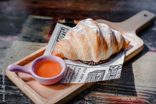 Croissant placed on paper with honey in a small cup ready to eat.