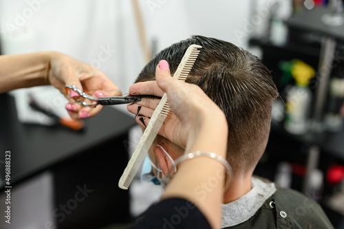A teenager in a beauty salon gets a haircut, a hairdresser cuts a teenage boy's hair.