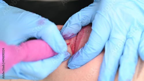 Skilled cosmetologist applying permanent makeup on lips in a beauty salon. Woman undergoing procedure of lip blushing with tattoo machine. Close-up