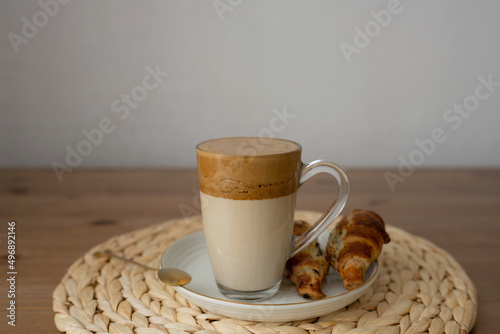 Dalgona coffee in a glass on a wooden table, with croissants.