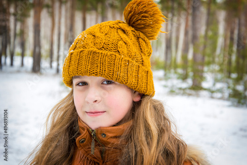 In winter, a beautiful girl with long hair in a hat with a balabon stands in the forest. photo