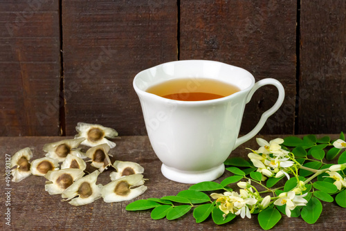Moringa Tea in white ceramic cup with fresh green leaf and flower on wooden background. Moringa oleifera tropical herb healthy lifestyle concept.