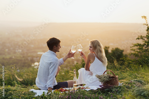 Beautiful young couple enjoying wine glasses and picnic day on the hill. Love and tenderness, dating, romance. Love concept. © eduard