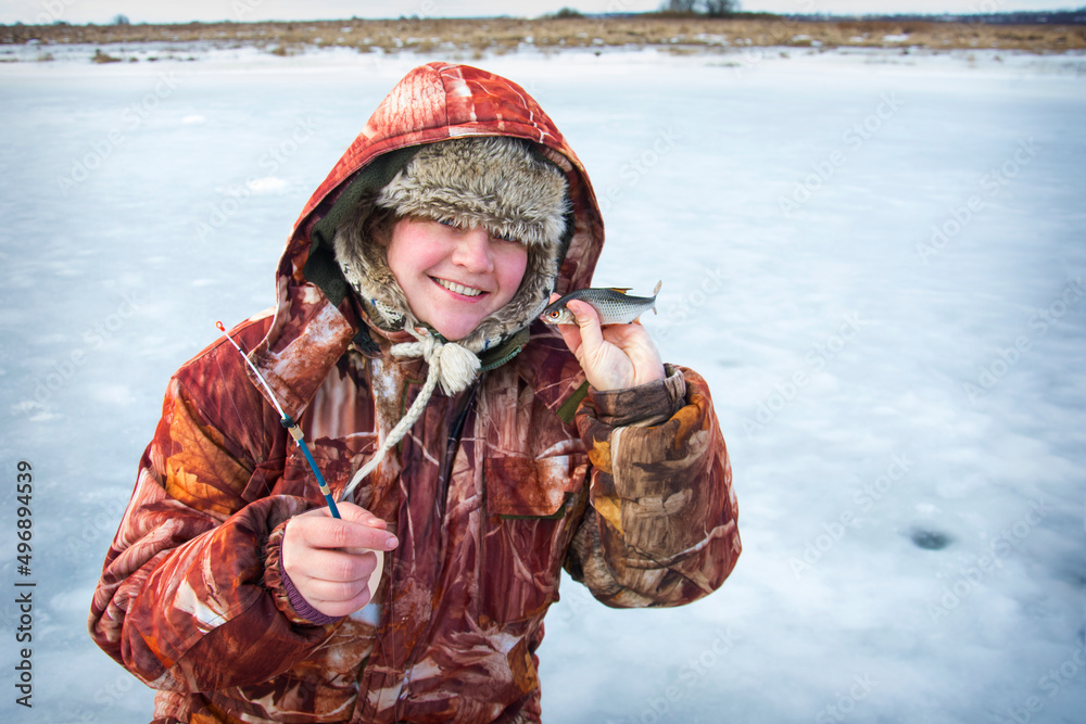 In winter, a girl in overalls caught a roach fish on the river.