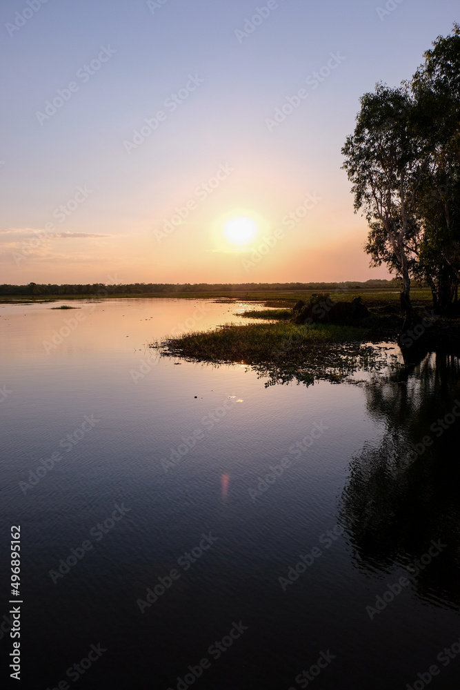 Obraz premium A beautiful, relaxing pastel coloured sunset reflecting on water surface and silhouetted trees in crocodile territory of Yellow Water, Northern Territories, Australia