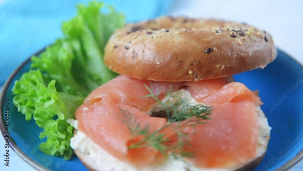 Multigrain bagel with cream cheese, salmon slices, dill and salad. Plate rotation, Slow motion. Multigrain bagel with cream cheese, salmon slices, dill and salad. Plate rotation, Slow motion.