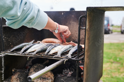 unrecognizable woman's hand filling barbecue grill with raw sardines and some bacon